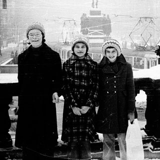 Three children pose in winter snow near historic city statue.