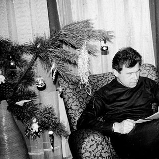 Man reading newspaper in armchair near Christmas tree.
