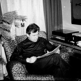 Man reading newspaper in armchair near Christmas tree.