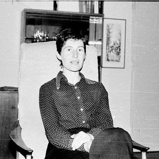 Woman sitting indoors in patterned blouse, smiling.