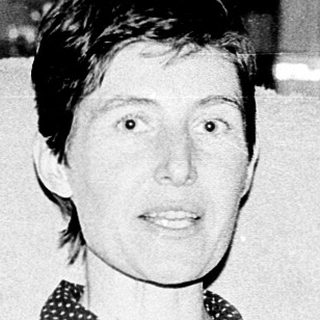 Woman sitting indoors in patterned blouse, smiling.
