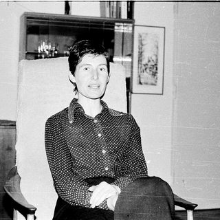 Woman sitting indoors in patterned blouse, smiling.