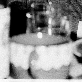 Elderly man seated at a table with wine bottle.