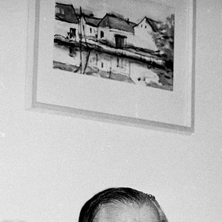 Elderly man seated at a table with wine bottle.