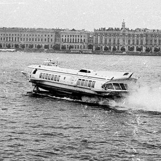 Fast boat on river near historic waterfront buildings.