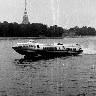 High-speed hydrofoil boat on water near spired buildings.