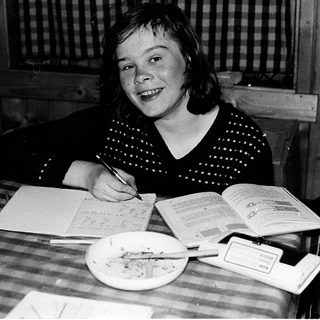 Young girl writing at a table with books.