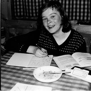 Young girl writing at a table with books.