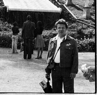 Man posing in park with grand staircase and statues.