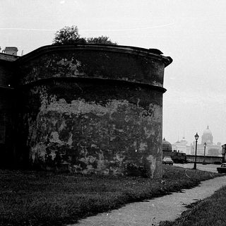 Historic city street with old fort wall, vintage cars, and distant cathedral.