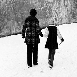 Two people walking together in snow-covered urban alley.