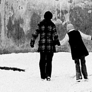 Two people walking in snowy alley beside wall.