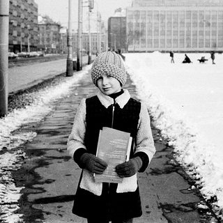 Child holding book on snowy urban street.