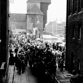 Crowded funeral procession through city street.