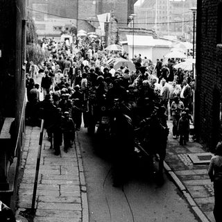 Crowded funeral procession through city street.