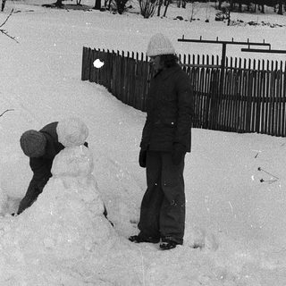 Snowman building in winter backyard scene.