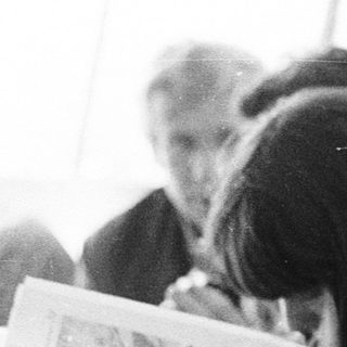 People reading newspapers in a crowded indoor setting.
