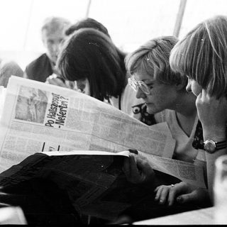 People reading newspapers in a crowded indoor setting.