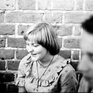 Young girl smiling indoors near brick wall.