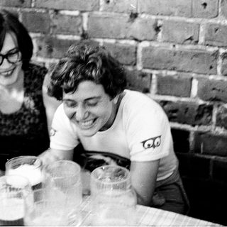 Two people laughing while sharing drinks indoors.