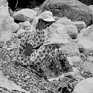 Person lying on gravel near seated individual.