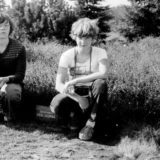 Two individuals sitting outdoors near a gravestone.
