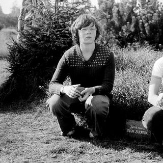 Two individuals sitting outdoors near a gravestone.
