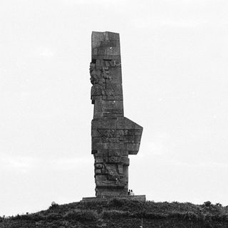 Tall concrete monument on hillside near water.