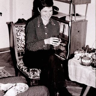 Woman knitting indoors near food and bookshelf.