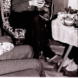 Woman knitting indoors near food and bookshelf.