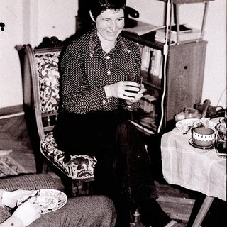Woman knitting indoors near food and bookshelf.