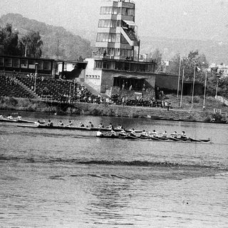 Rowing team competing on a river near stadium.