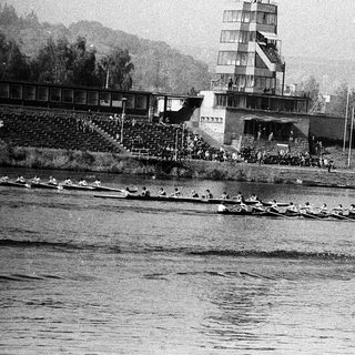 Rowing team competing on a river near stadium.