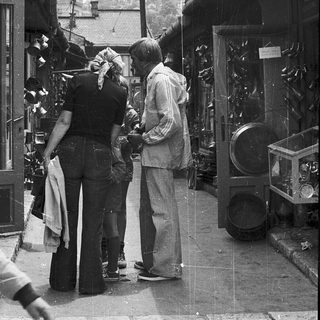 People examining vintage clocks in a street shop.