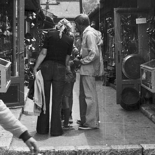 People examining vintage clocks in a street shop.