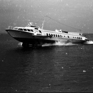 Ferry boat navigating rough seas near coastline.