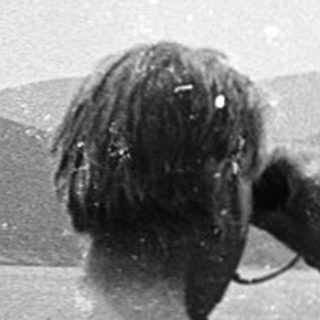 Shirtless man taking photo of rocky island in snowy coastal landscape.