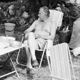 Shirtless man relaxing in folding chair outdoors.