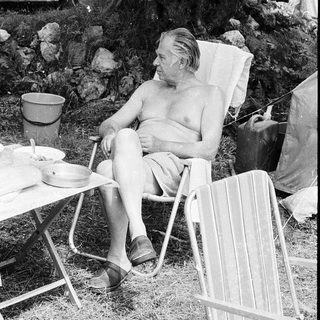 Shirtless man relaxing in folding chair outdoors.