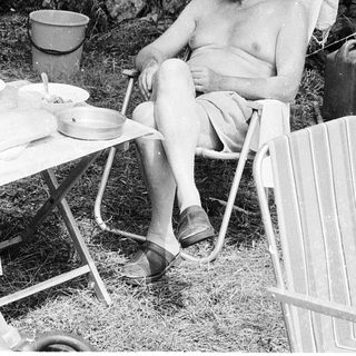 Shirtless man relaxing in folding chair outdoors.