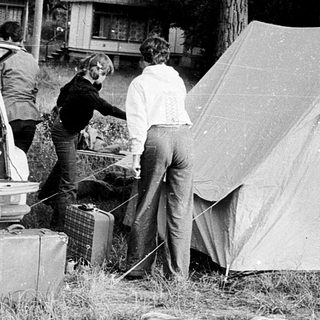 People setting up a tent near parked cars.