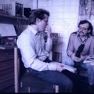 Two men discussing in a retro office workspace.