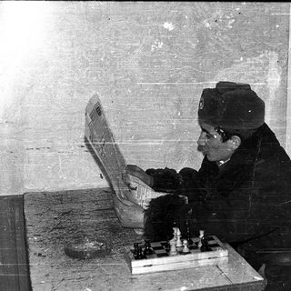 Old man playing chess with laptop open.