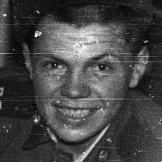 Young soldier in wartime uniform smiling indoors.