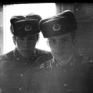 Two soldiers in uniform pose near a window.