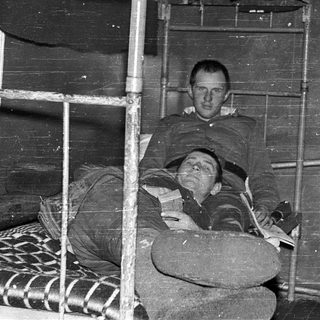 Two men resting on bunk beds in confined quarters.