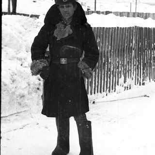 Person in winter military attire standing outdoors in snow.