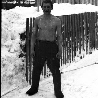 Shirtless boy standing in snowy outdoor setting.
