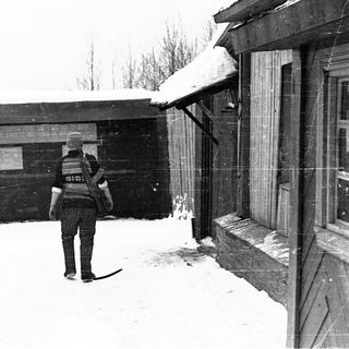 Person in winter uniform walks through snowy courtyard.