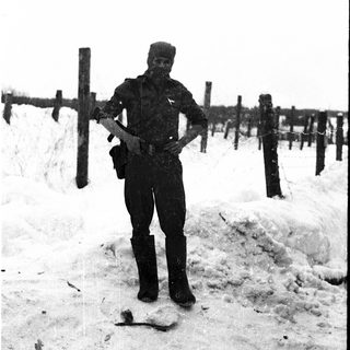 Soldier in winter uniform standing near barbed wire.